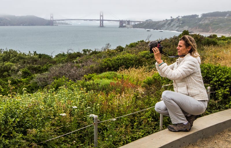 woman taking photo of san francisco bay with fog covered golden gate bridge in distance