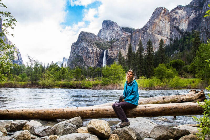 woman sitting on a log with water and mountains in the background