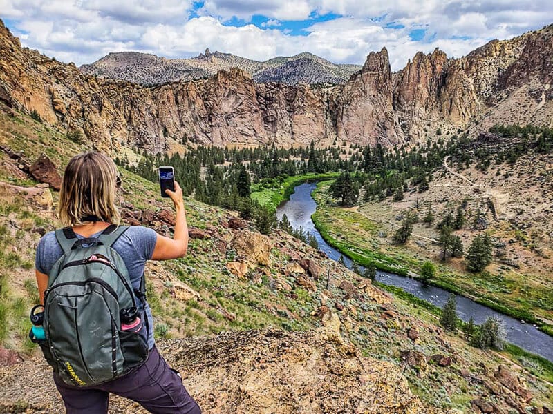 woman taking photo of jagged mountains and river running through valley