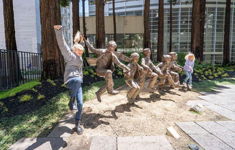 girls jumping next to statues