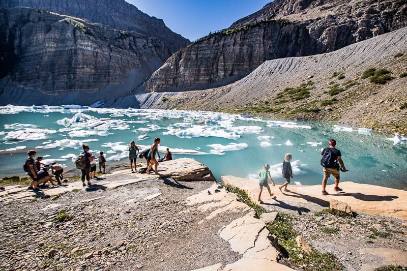 people looking astatine  torquise water  with icebergs astatine  Grinnell Glacier Trail