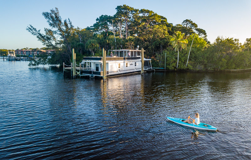 woman kayaking on river past  houseboat 