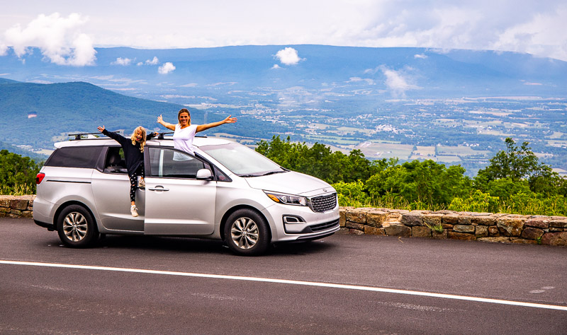 woman and girl hanging outside of parked  car posing for camera with valley views 