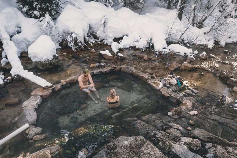 two people sitting in natural hot springs surrounded by snow