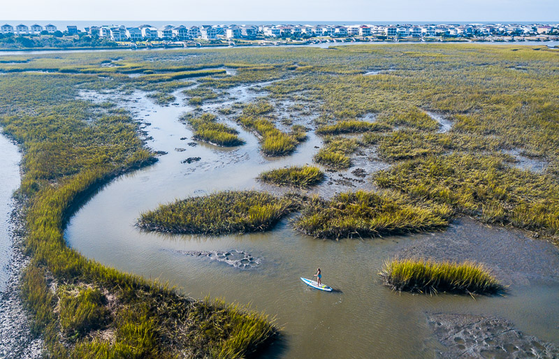aerial of woman Stand up paddle boarding, on salt marshes