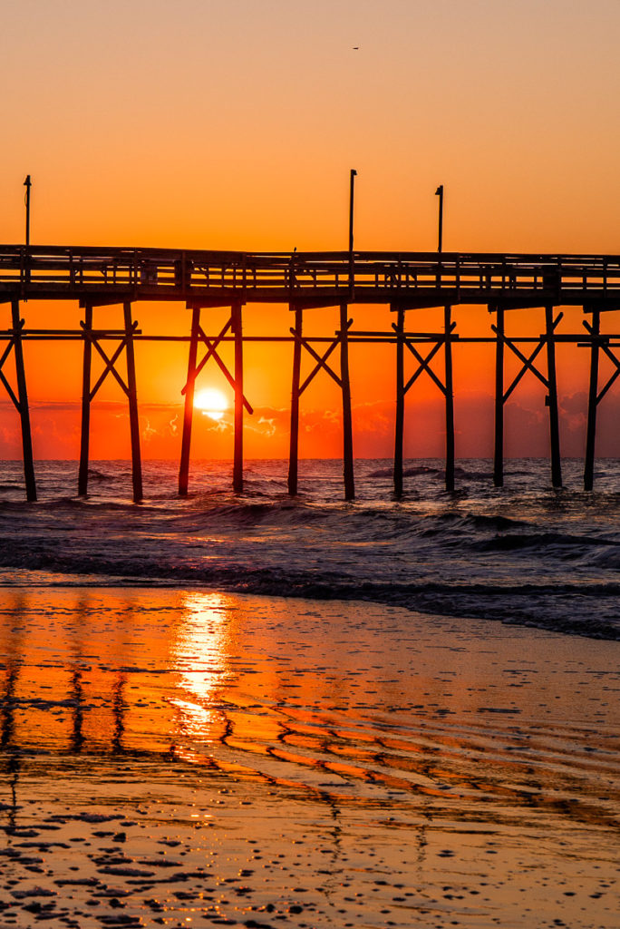 orance sunrise with sun poking between pier legs