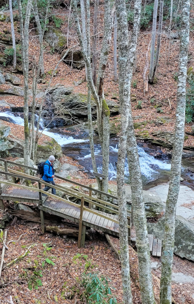 man walking down stairs in a wooded area next to a waterfall