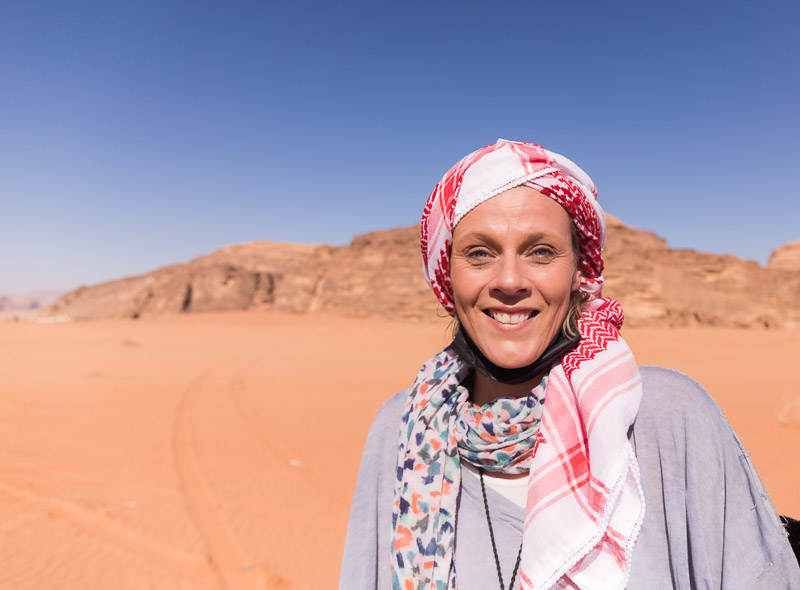 woman wearing beduoin scarf in desert smiling at camera