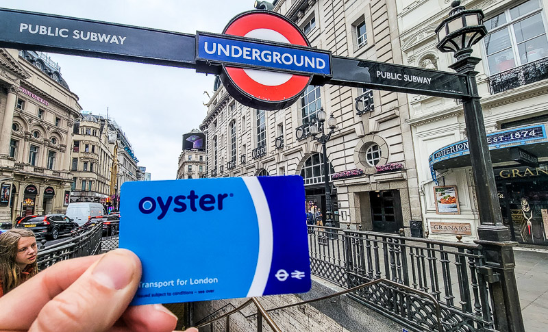 person holding up oyster card out front of tube station