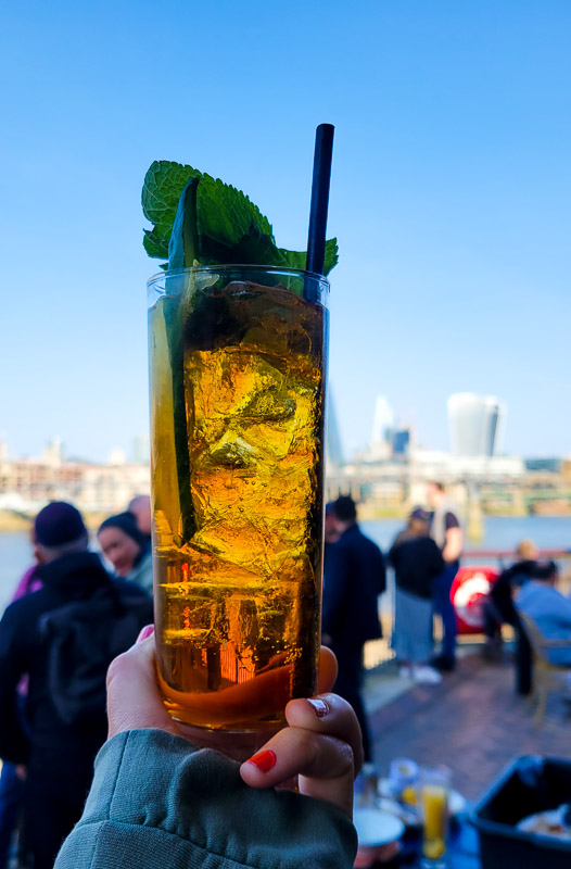 hand holding pimm's and lemonade with views of london successful  background