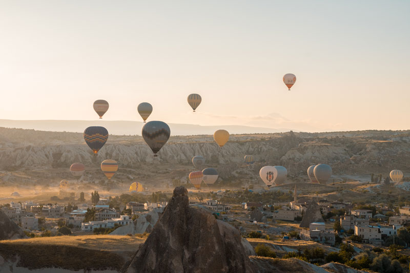 sky full of hot air balloons rising up from the desert landscape of Cappadocia at sunrise