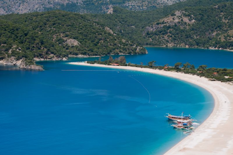 brilliant blue water, sweeping white sandy Oludeniz beaches and a lagoon framed by small hills dotted with trees in Fethiye Turkey