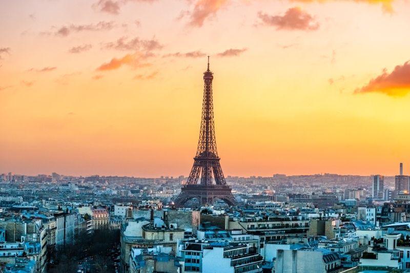 view of Eiffel tower rising above the city buildings with an orange sunset sky