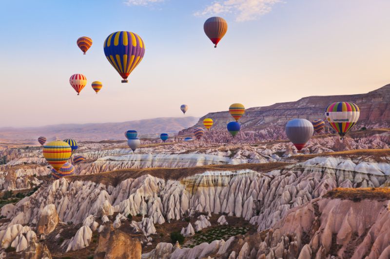 scores of hot air balloons rising into the sky  at sunrise over the rocky valley of Cappadocia