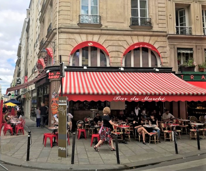 A woman walking past a cafe with people sitting in front in Paris