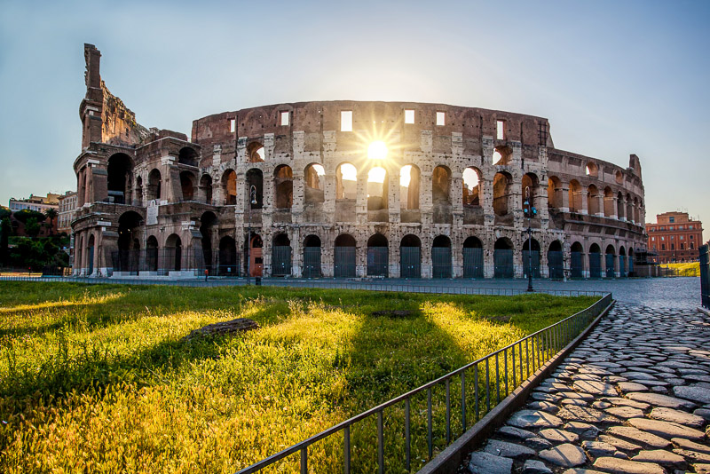 the outer walls of the colosseum with the rising sun bursting through