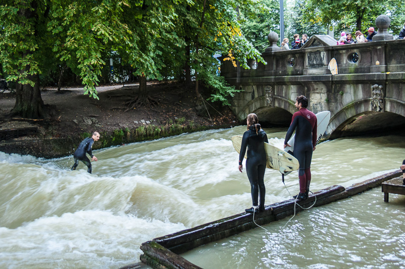 Surfer riding a wave on the Eisbach River Munich while two surfers stand watching