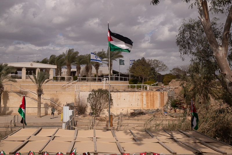 small jordna river with building and flags of isreal and palestine flying
