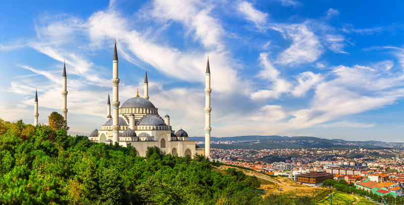 white mosque with turrets on green hillside with views of Istanbul