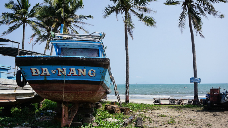 boat with dan nang written on it on the beach with palm trees