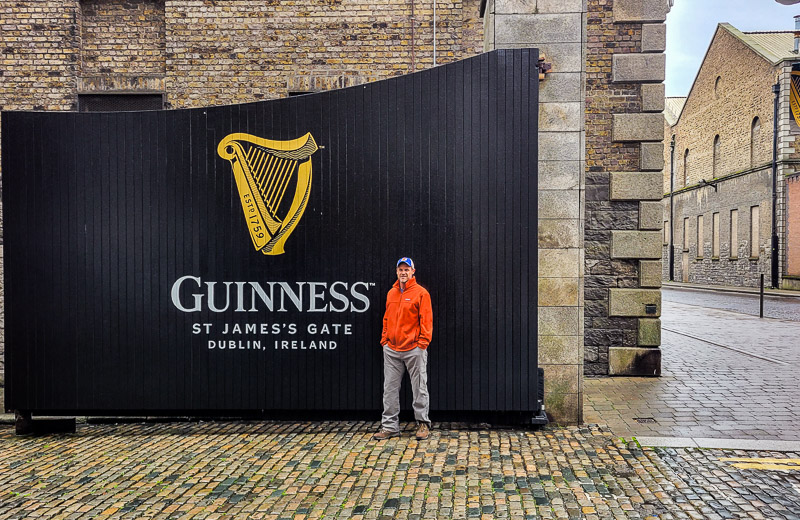 Person standing in front of a large black gate with the name Guinness on it