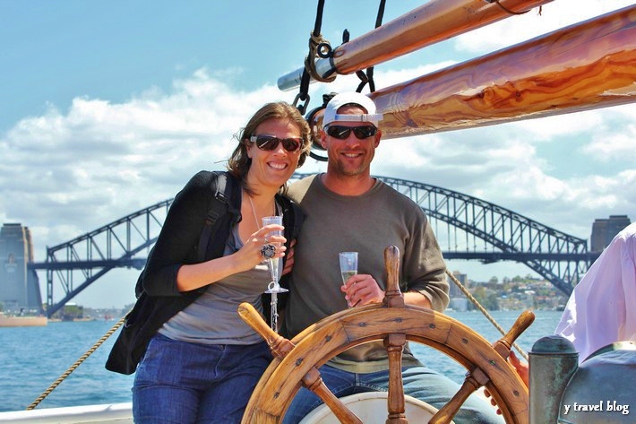 man and woman drinking champagn behind the steering wheel of tall ship in sydney harbor