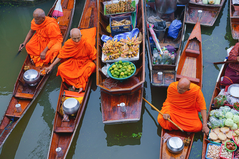 buddhist monk rowing wooden boat in canal with alms bowl at Tha Kha floating market