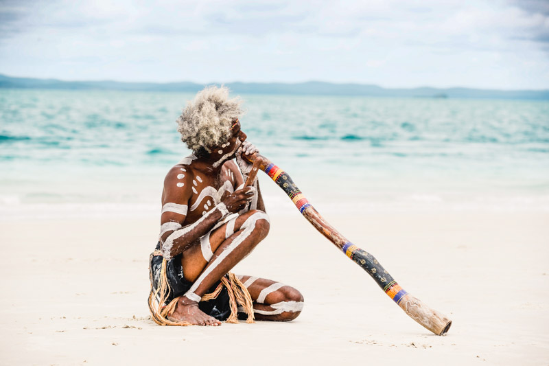 aboriginal man playing didgeridoo on the beach