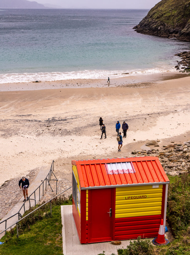 A beach with a lifesaver shed, and people walking up the path