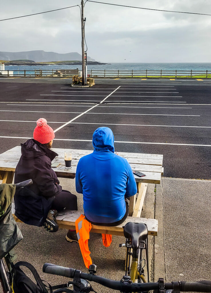 Two people sitting outisde a pub drinking a beer with water views