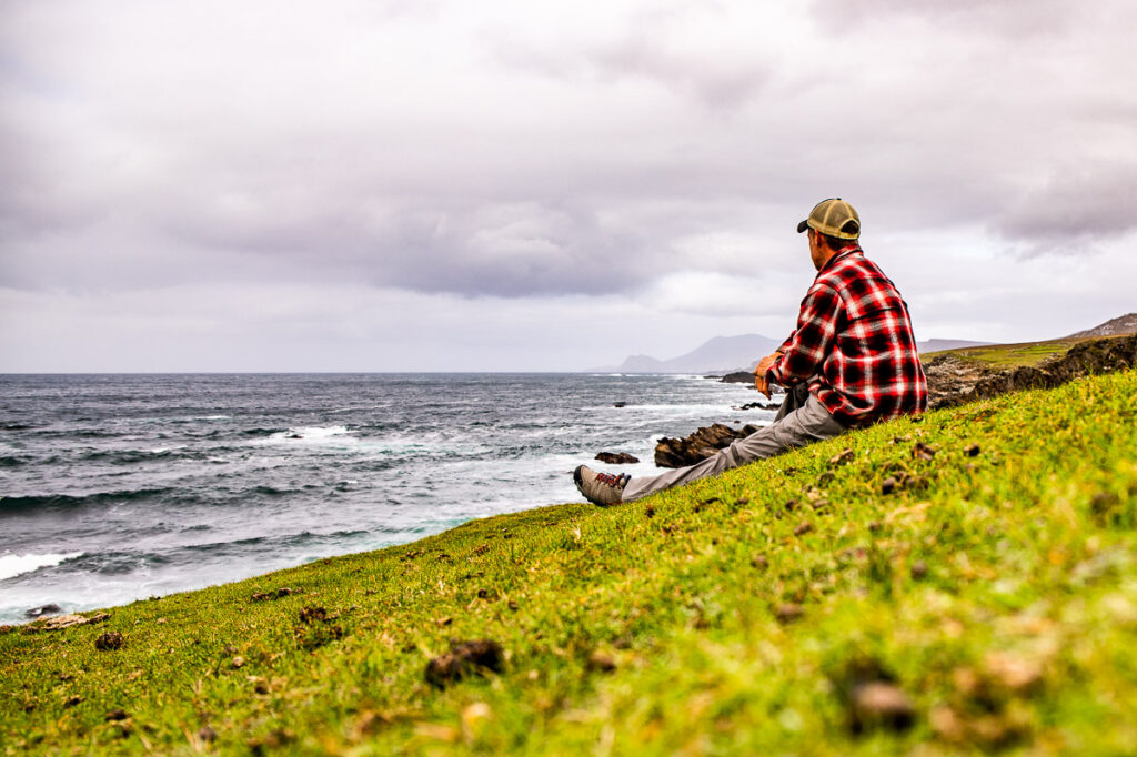 Man sitting on a grassy hill overlooking the ocean