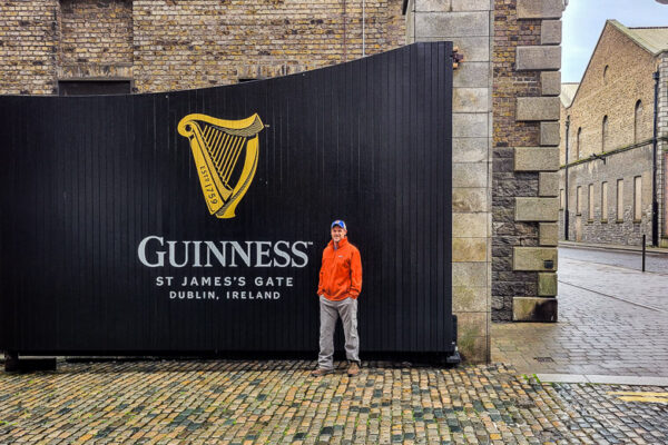 Man standing in front of a large black gate with the words Guinness
