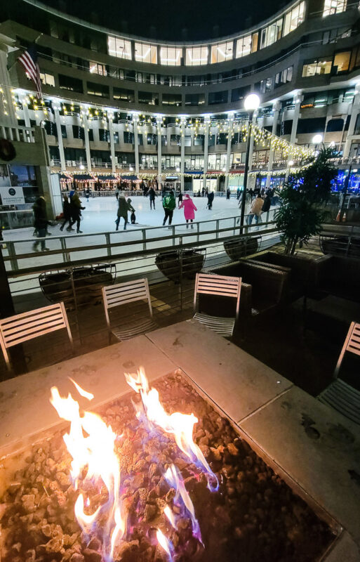 People ice skating inside a rink with a fire pit