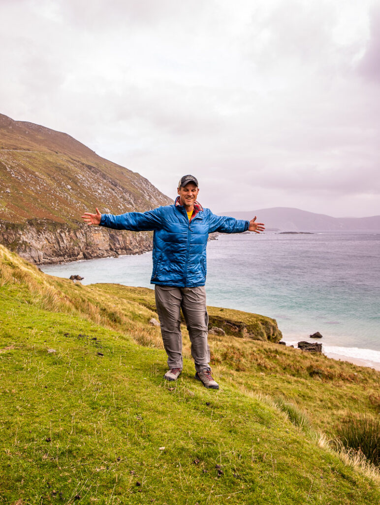 Man standing on grassy cliff overlooking a beach