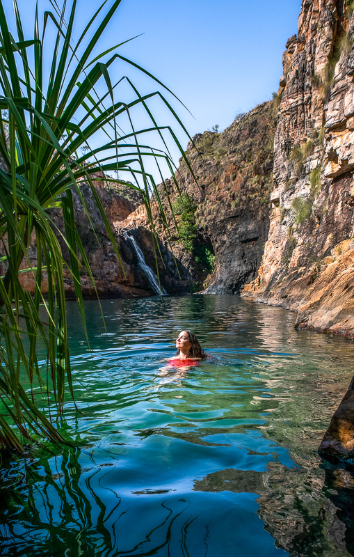 person swimming in pristine waterhole surrounded by rock walls at Maguk or Barramundi gorge