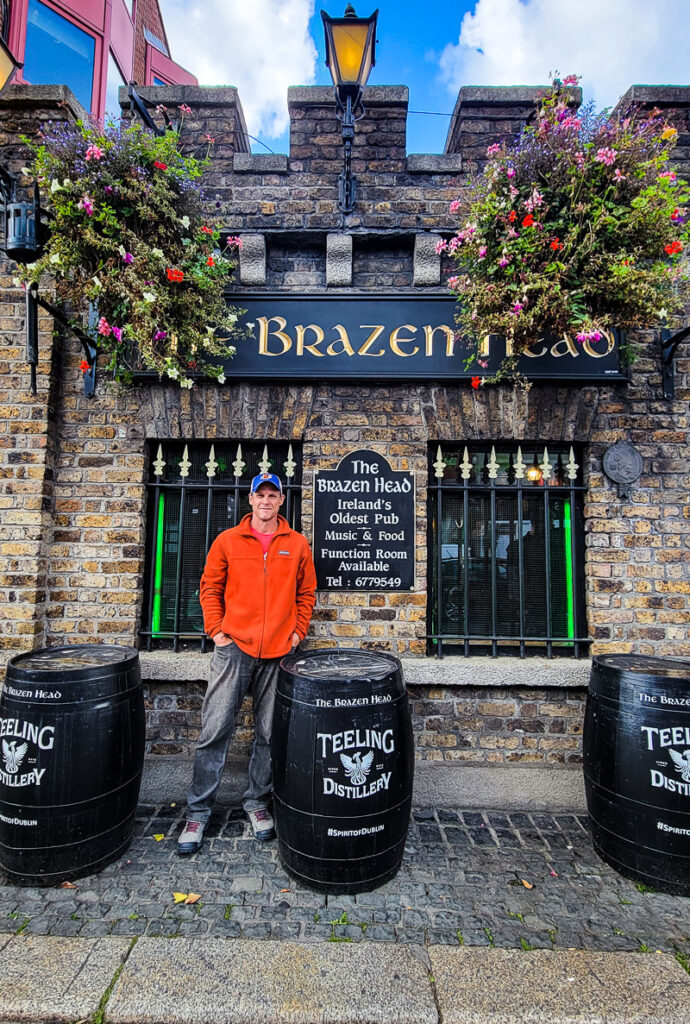 Man standing outside the entrance to a pub with two wine barrels