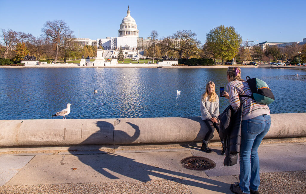 Mom and daughter taking photo in front of a pond and US Capitol Builing in Washington DC