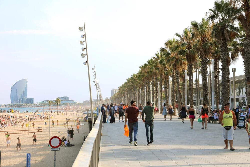 Promenade of Barceloneta beach with people enjoying a sunny day in Barcelona.