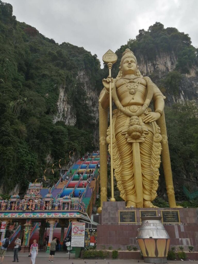 golden buddha statue beside colorful steps to batu cave