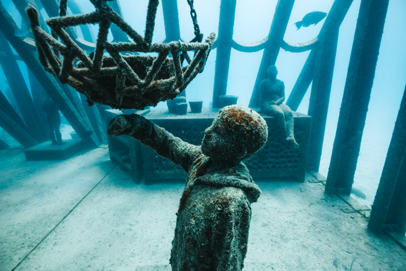 underwater sculpture of boy looking at shipwreck