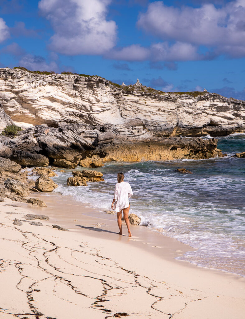 Lady walking along a beach towards a rocky headland