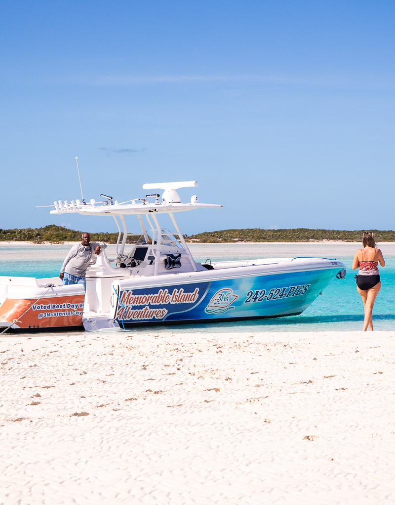 Boat anchored on the edge of a beach with a lady standing next to it