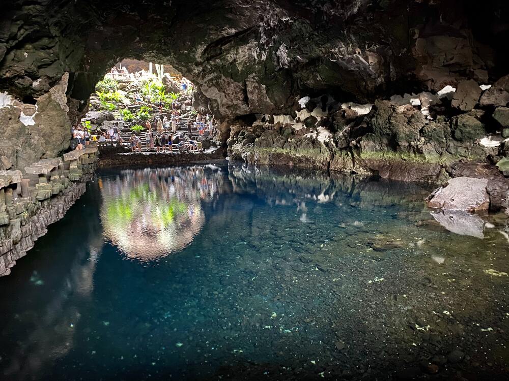 people standing in cave entrance looking at pool of water