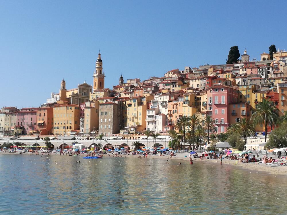people on beach and colorful buildings of menton