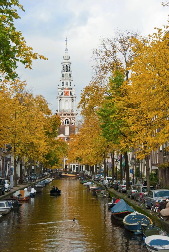 boat going down Amsterdam canal with autumn foliage on thebanks and church steeple