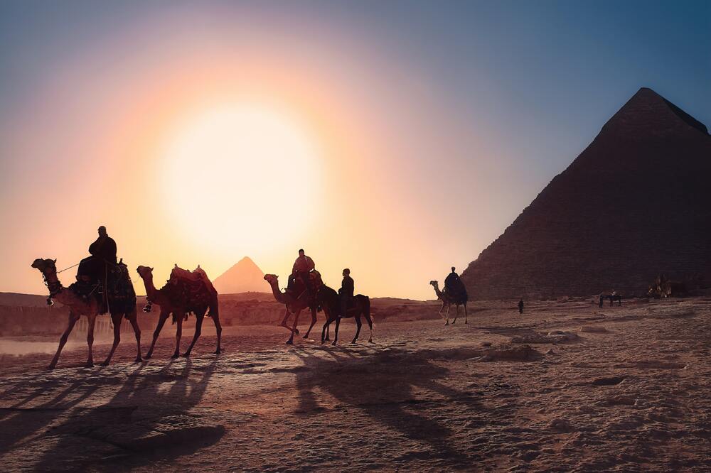 people riding camels at sunrise in front of the pyramids