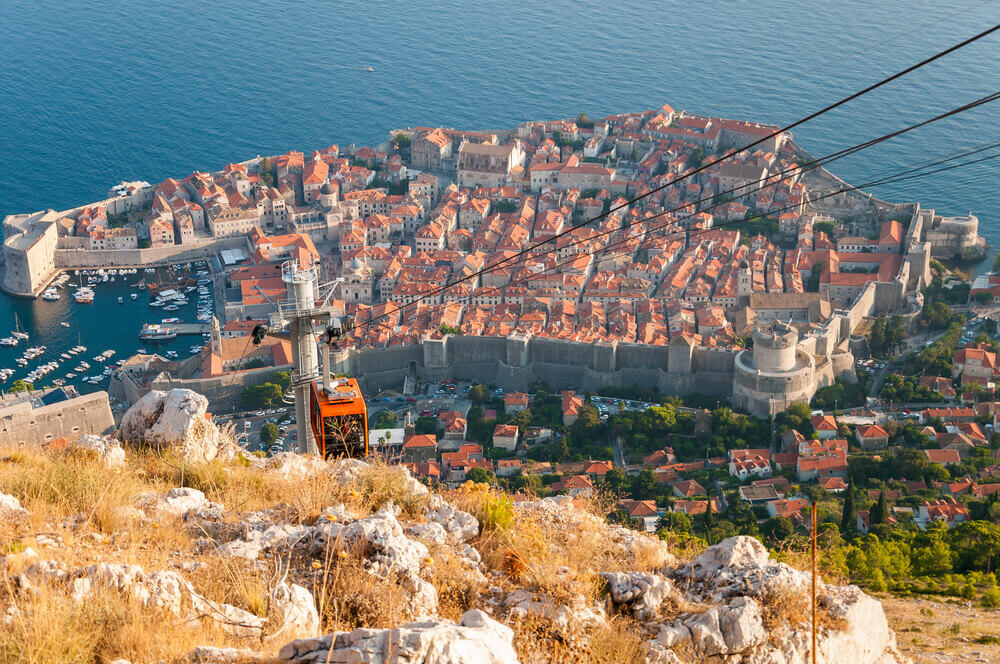 aerial view of cable car going up hill with orange roofed homes surrounded by the old city walls