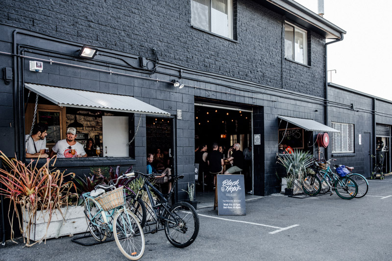 bicycles against black building with brewery garage doors open and people drinking