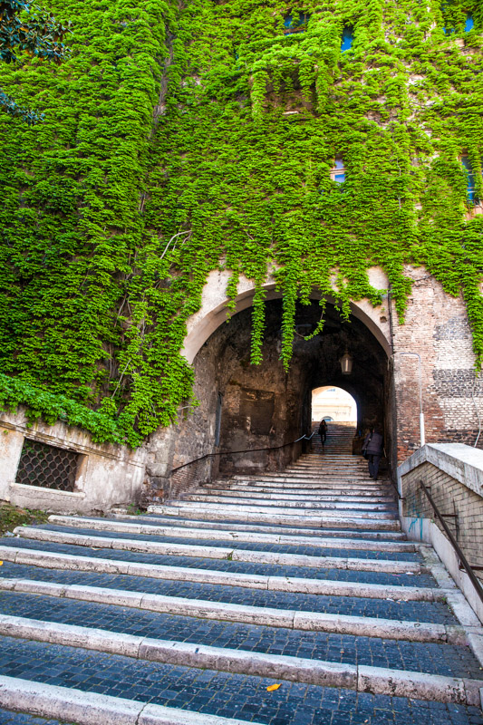 stairs going up to vine covered stone building. The famous Borgia Ascent in the Monti neighborhood of Rome