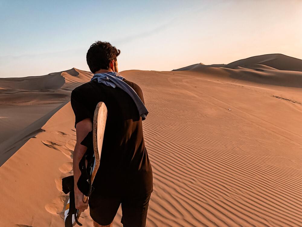 man carrying sandboard up the dunes